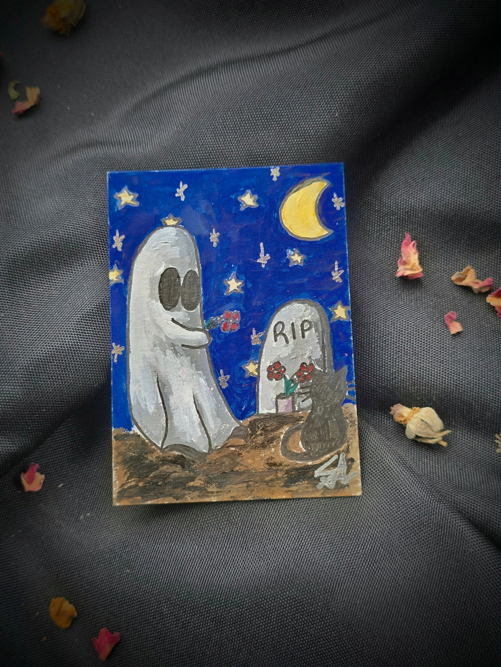 A Little Forever original Ghost and Kitty ACEO painting showing a white ghost holding flowers beside a black cat and gravestone, styled on black fabric with dried rose petals.