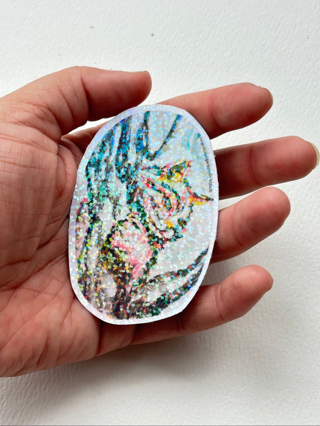 Between The Branches 3-inch cat vinyl sticker held in hand to show size and holographic finish