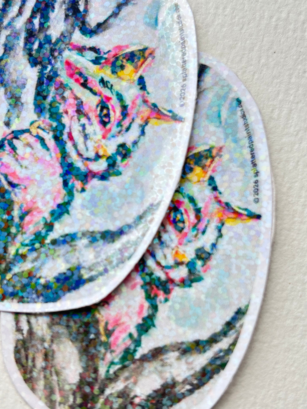 Two Between The Branches cat stickers overlapping to show the colorful holographic finish