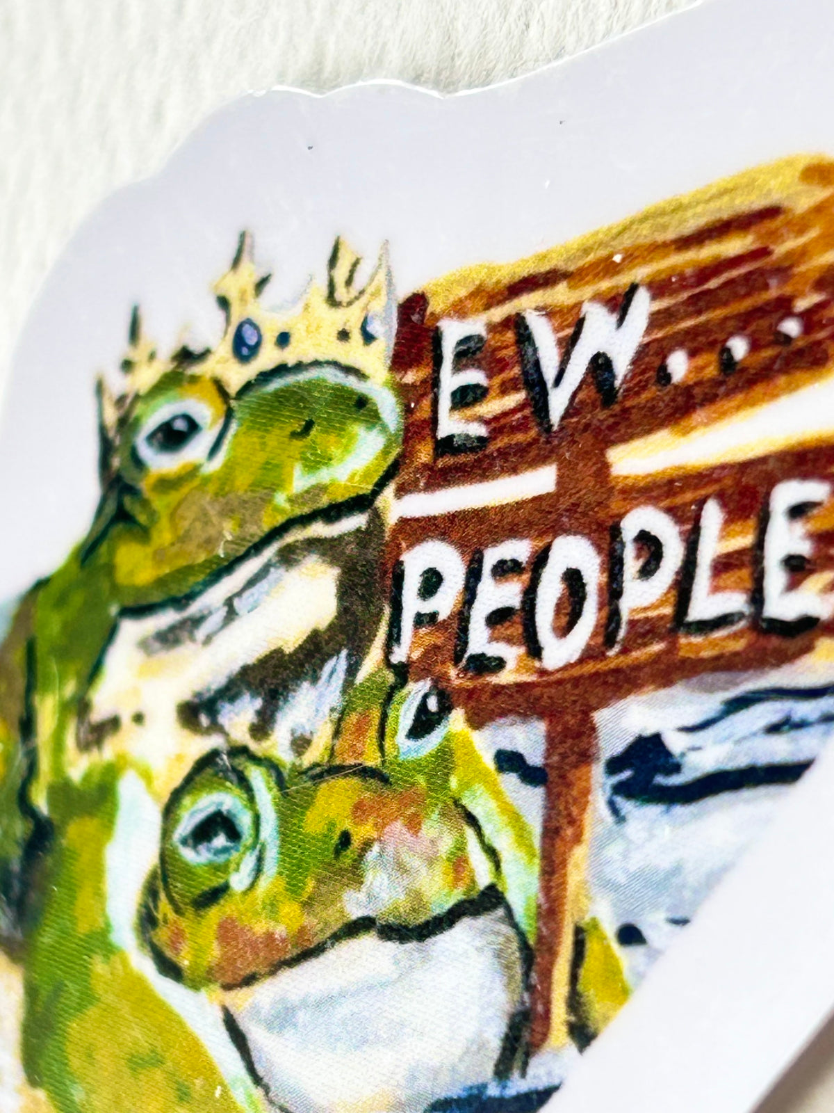 Close-up of Ew...People vinyl sticker showing two green frogs beside the hand-painted Ew People sign