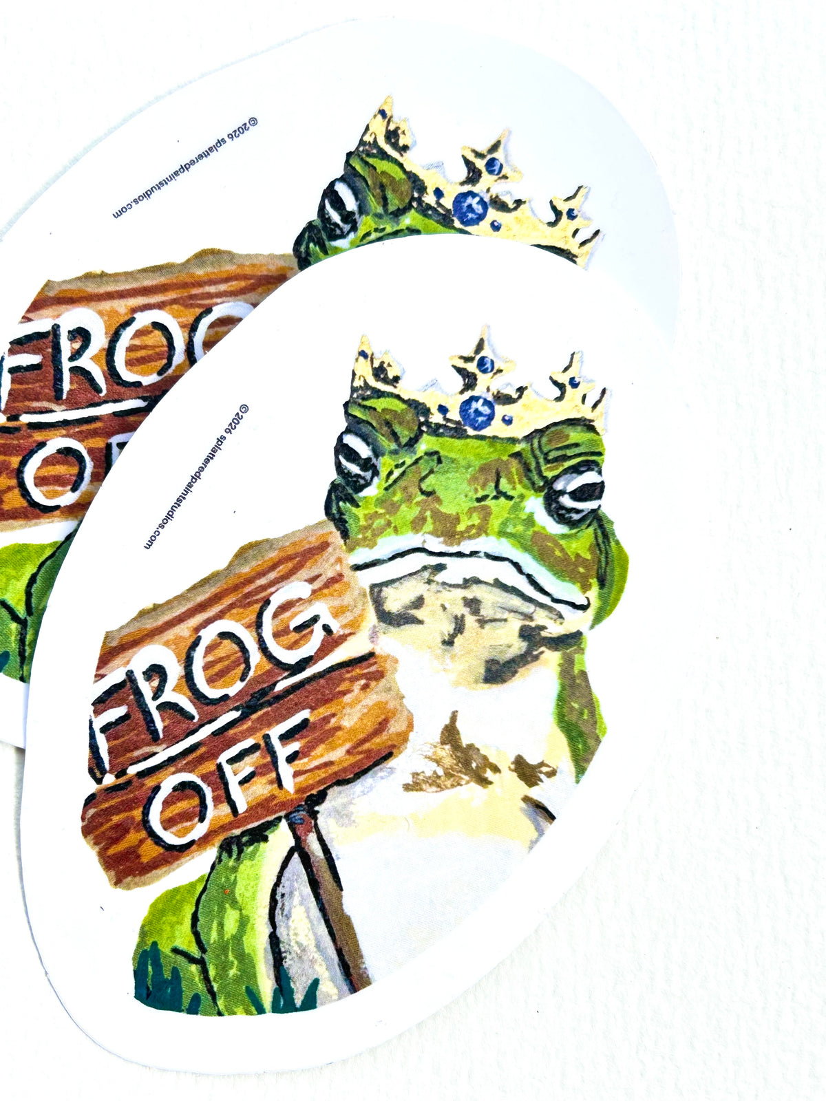 Stack of Frog Off vinyl stickers featuring a crowned green frog holding a wooden Frog Off sign