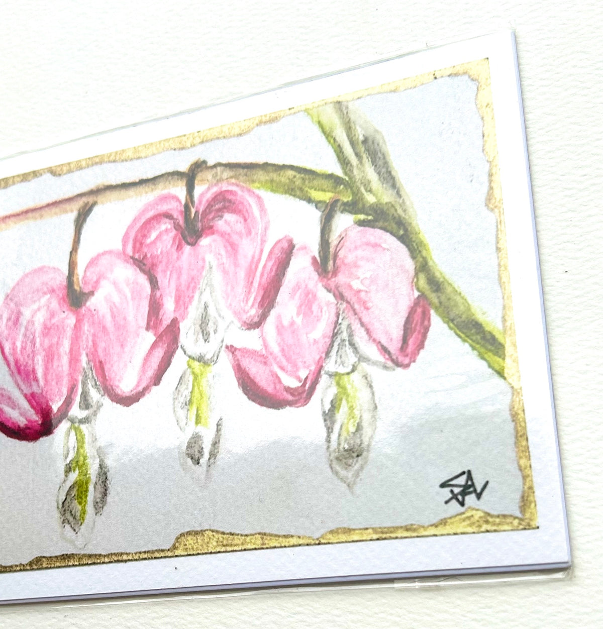 Angled close-up of Hearts in Bloom 5x7 art print showing pink bleeding heart flowers, gold border, and artist mark