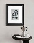 Looking Back 5x7 charcoal art print displayed framed above a small table with coffee