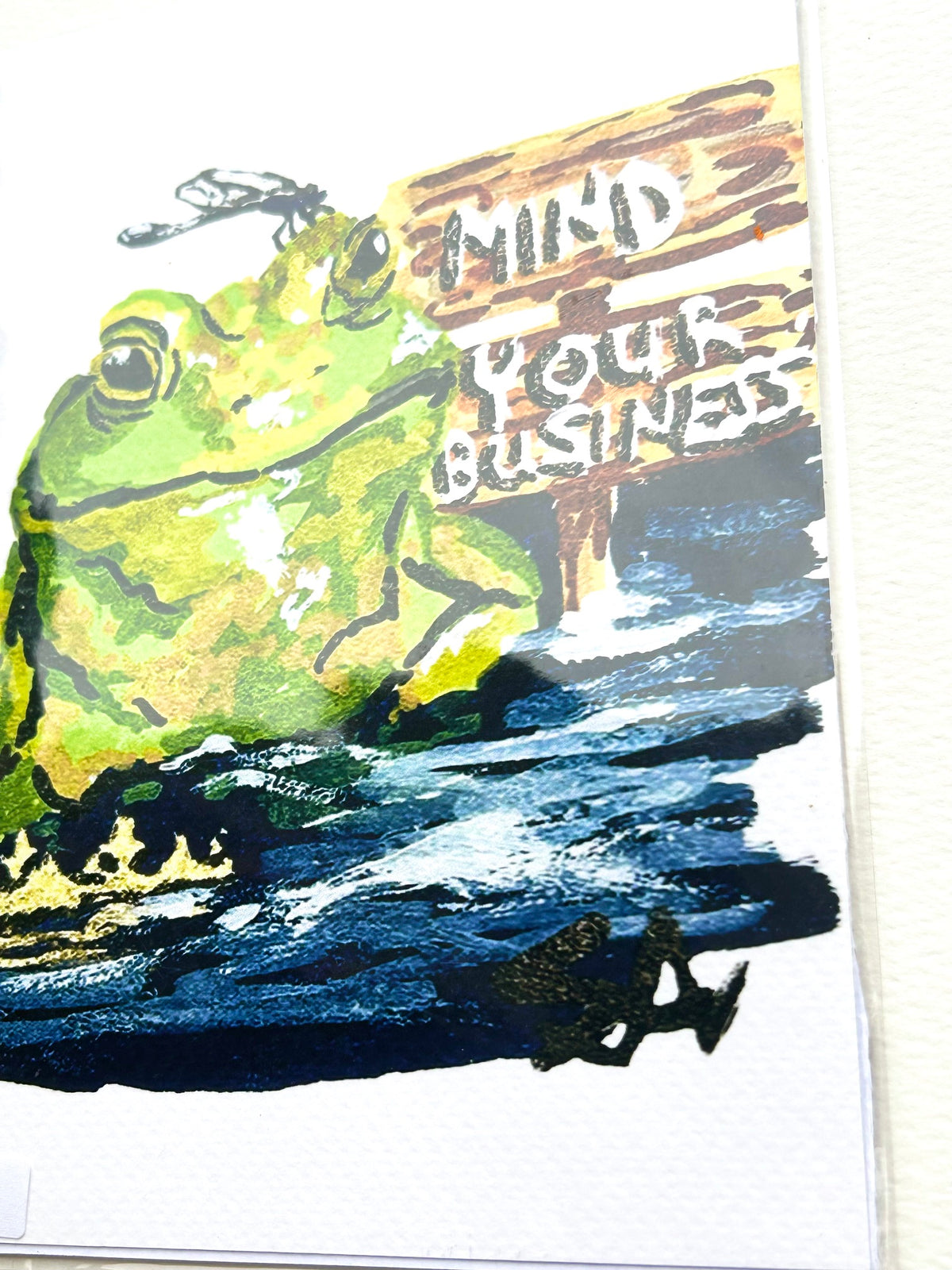 Angled detail of Mind Your Business 5x7 frog art print showing the green frog, sign, dragonfly, and blue water