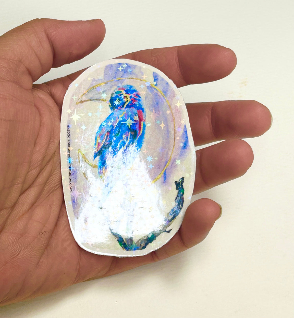 Moonbound Sentinel 3-inch holographic vinyl art sticker held in hand to show size and reflective finish