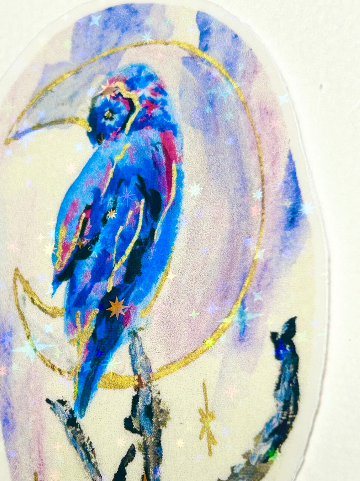 Full view of Moonbound Sentinel holographic vinyl sticker featuring a vivid blue bird with gold moon and reflective star accents
