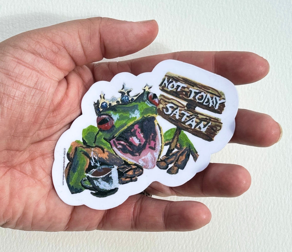 Not Today Satan 3-inch vinyl frog sticker held in hand to show size and scale