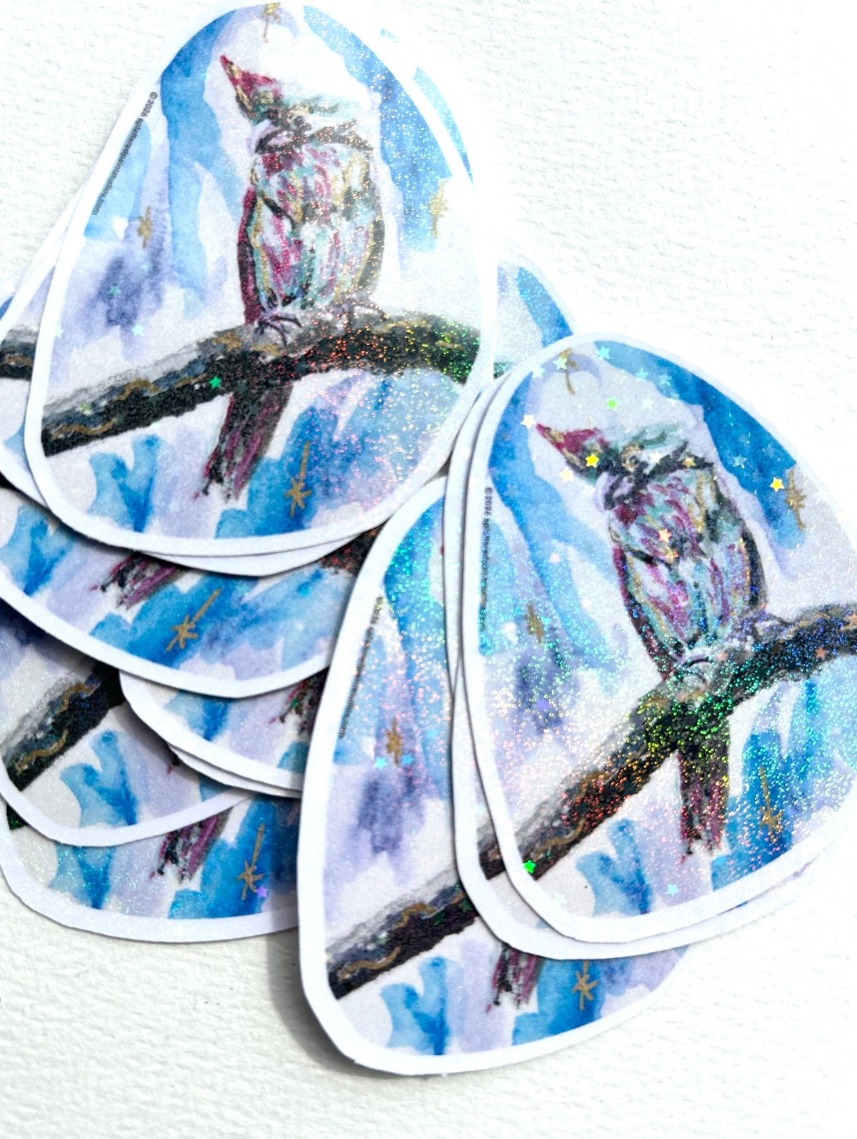 Stack of Starward Vigil vinyl stickers featuring a colorful parrot with shimmering celestial details