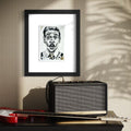 The Showman expressive black and white portrait art print with gold accents displayed in a black frame above a guitar amplifier.