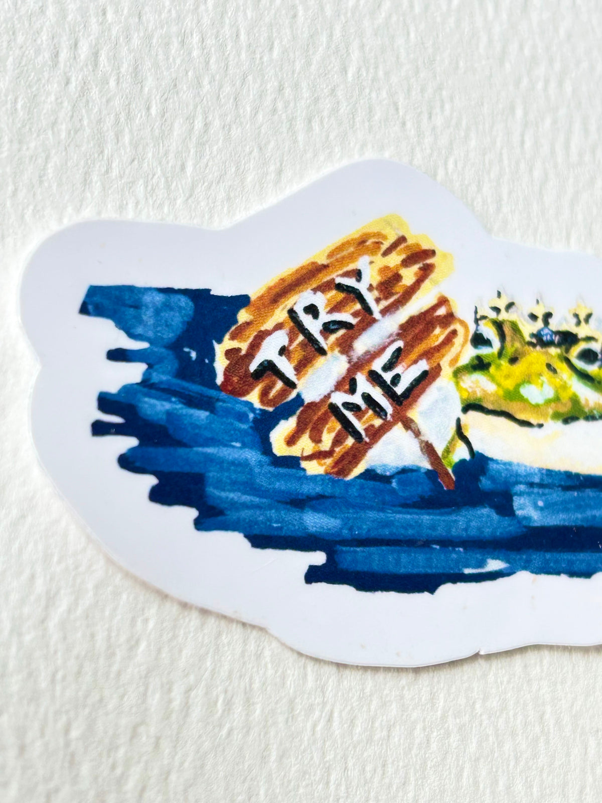 Angled view of Try Me vinyl sticker featuring a crowned frog beside a painted Try Me sign