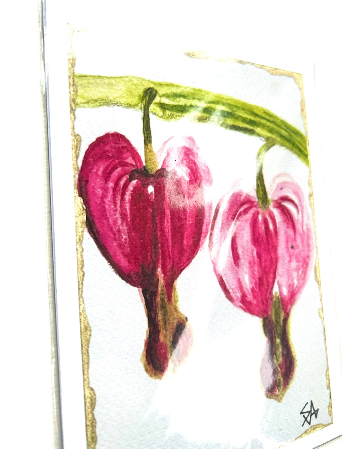 Angled detail of Twin Devotion 5x7 art print showing two pink bleeding heart flowers, green stems, and gold border